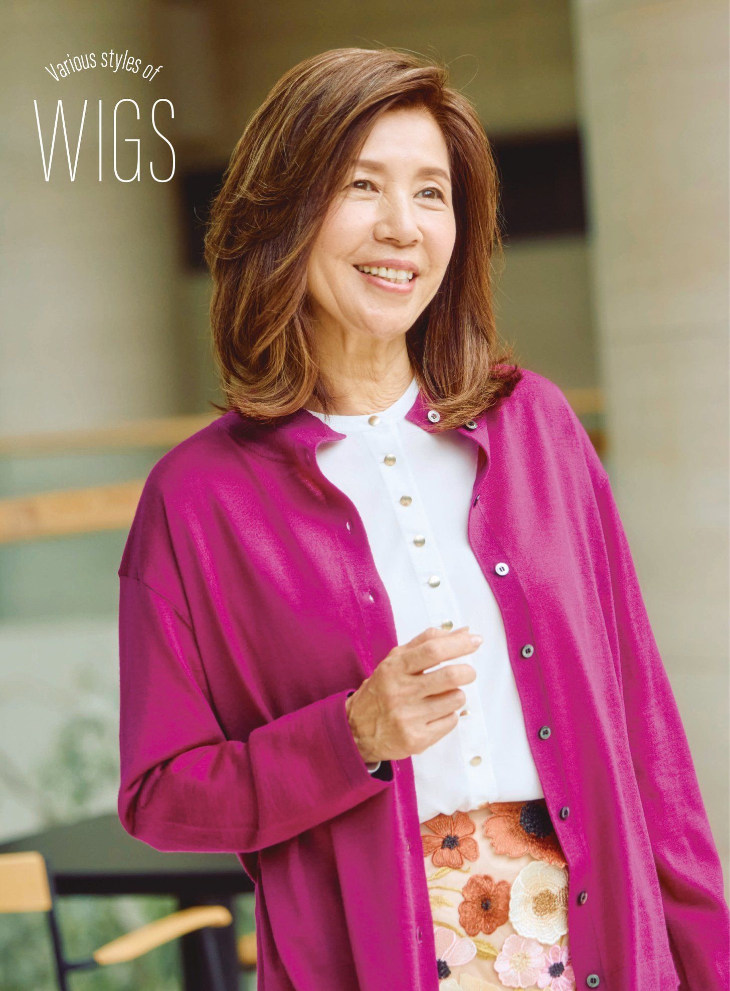 Various styles of WIGS。ピンクのカーディガンに花柄のスカートを合わせ、前髪なしのセミロングでほほえむ冨田由美子さん